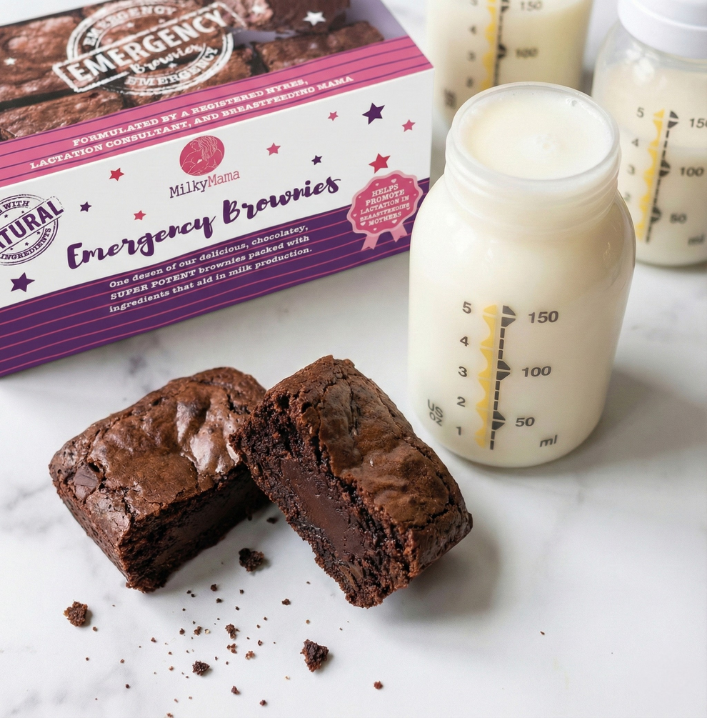 Chocolate brownies with a box of 'Emergency Brownies' and bottles of milk on a marble surface.
